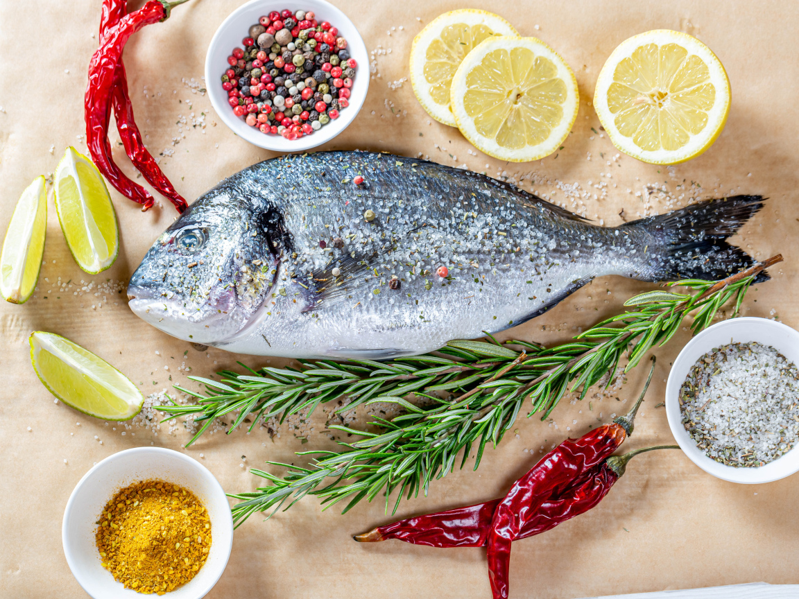 Свежая рыба на столе со специями, лимоном, розмарином и красным перцем