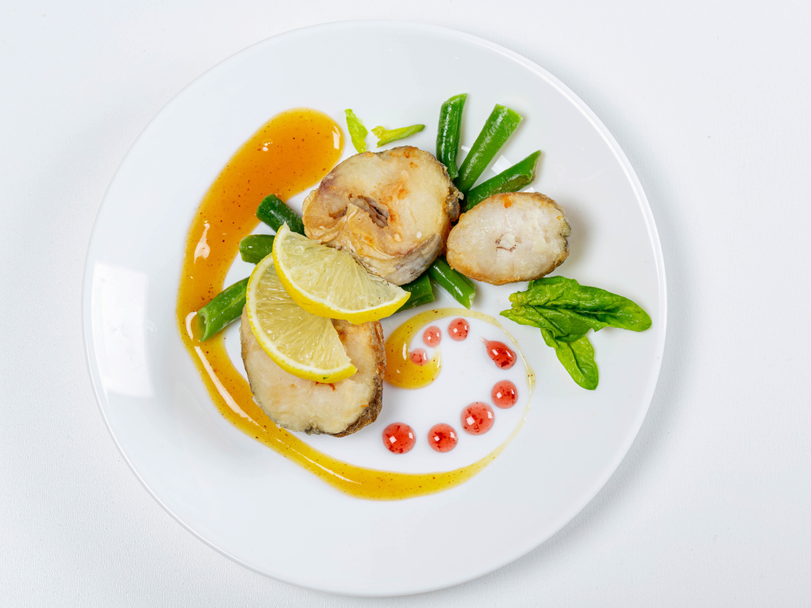 Кусочки жареной рыбы на белой тарелке с лимоном и зеленью