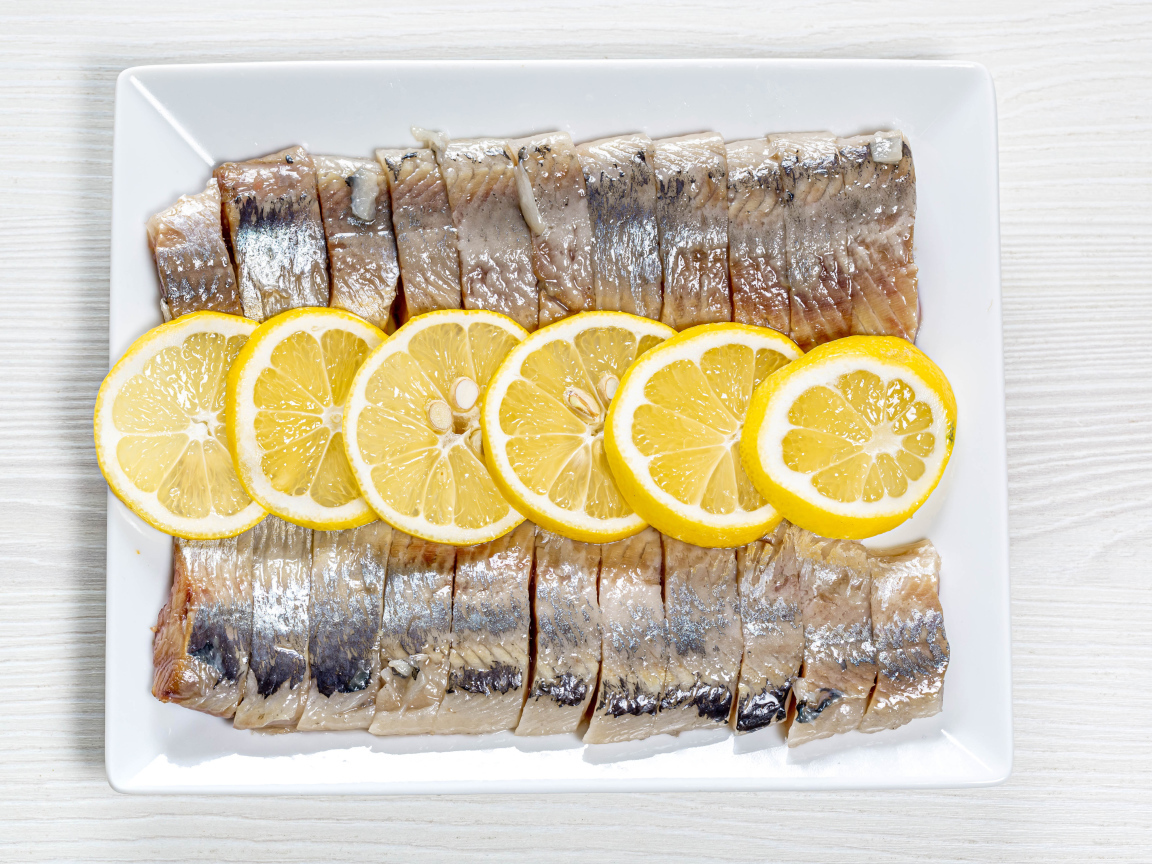 Sliced herring on a white plate with lemon