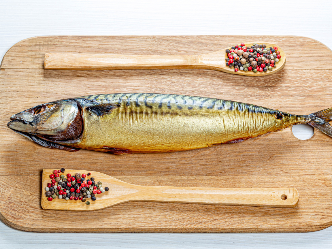 Копченая скумбрия на разделочной доске с перцем на белом фоне