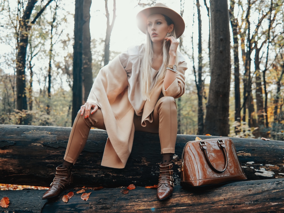 Девушка в пальто сидит на упавшем дереве в лесу 