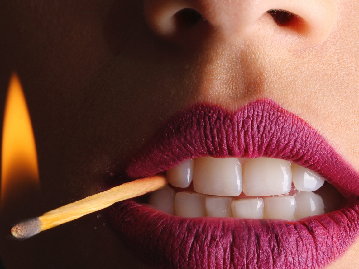 Зажженная спичка в зубах у девушки 