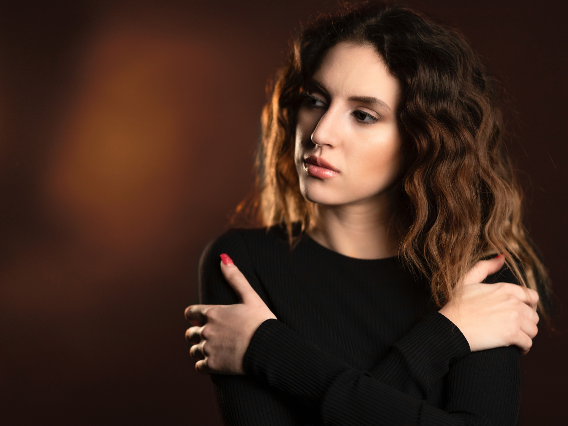 Молодая девушка стоит у стены в черном свитере