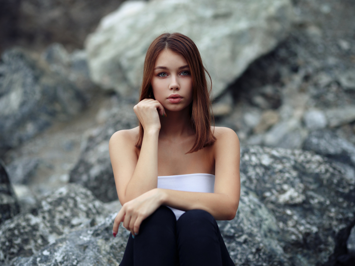 Молодая девушка сидит на камнях 