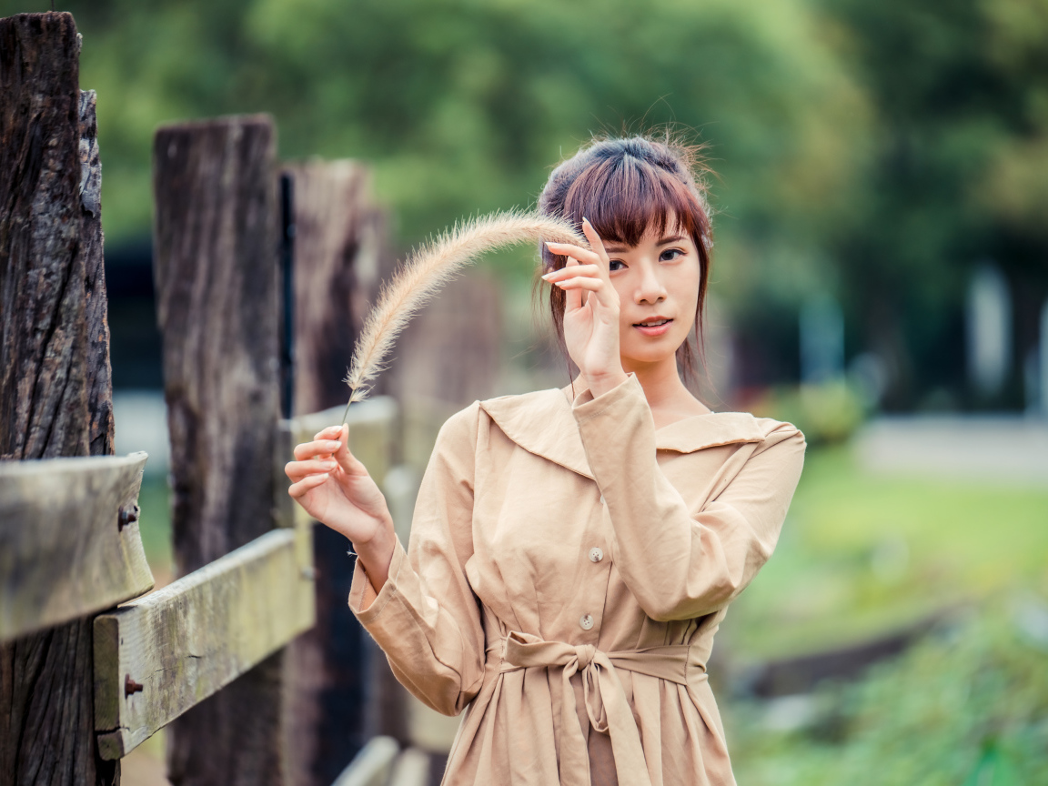 Девушка азиатка в пальто стоит у забора 