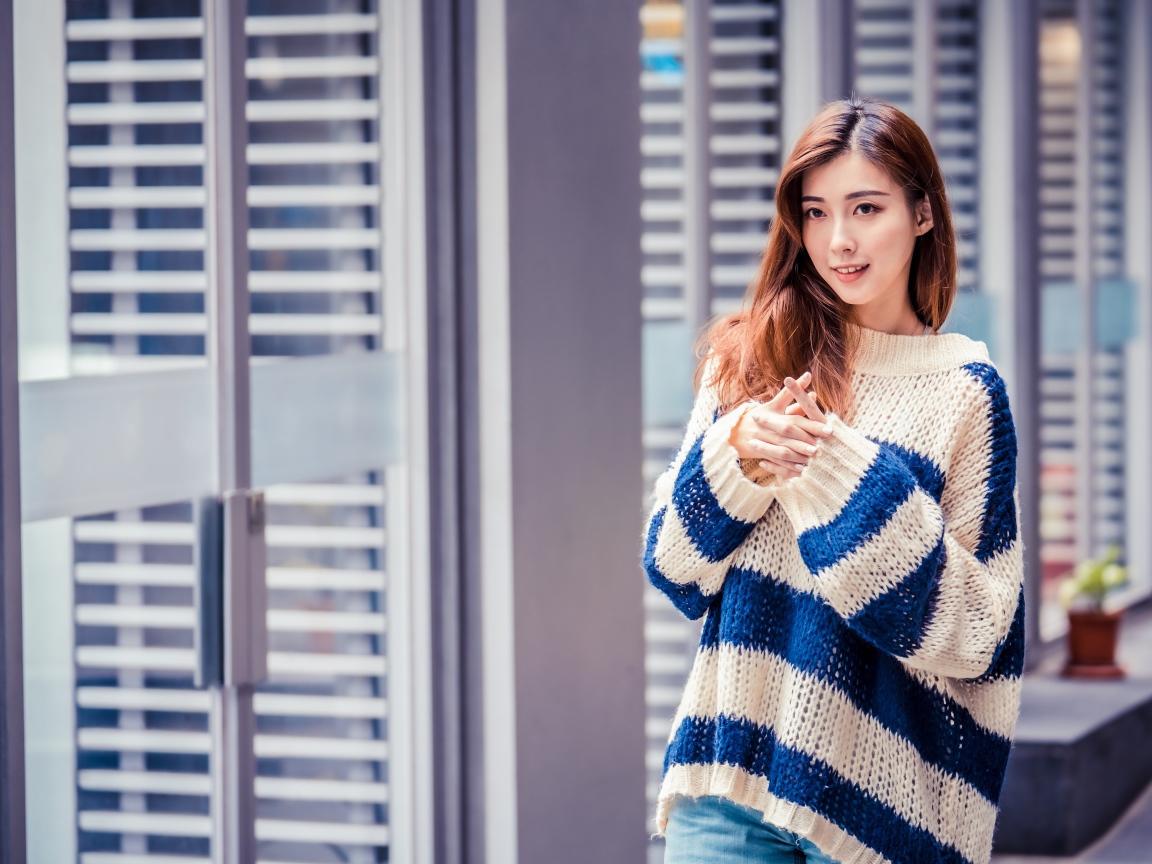 Девушка азиатка в теплом свитере стоит у окна