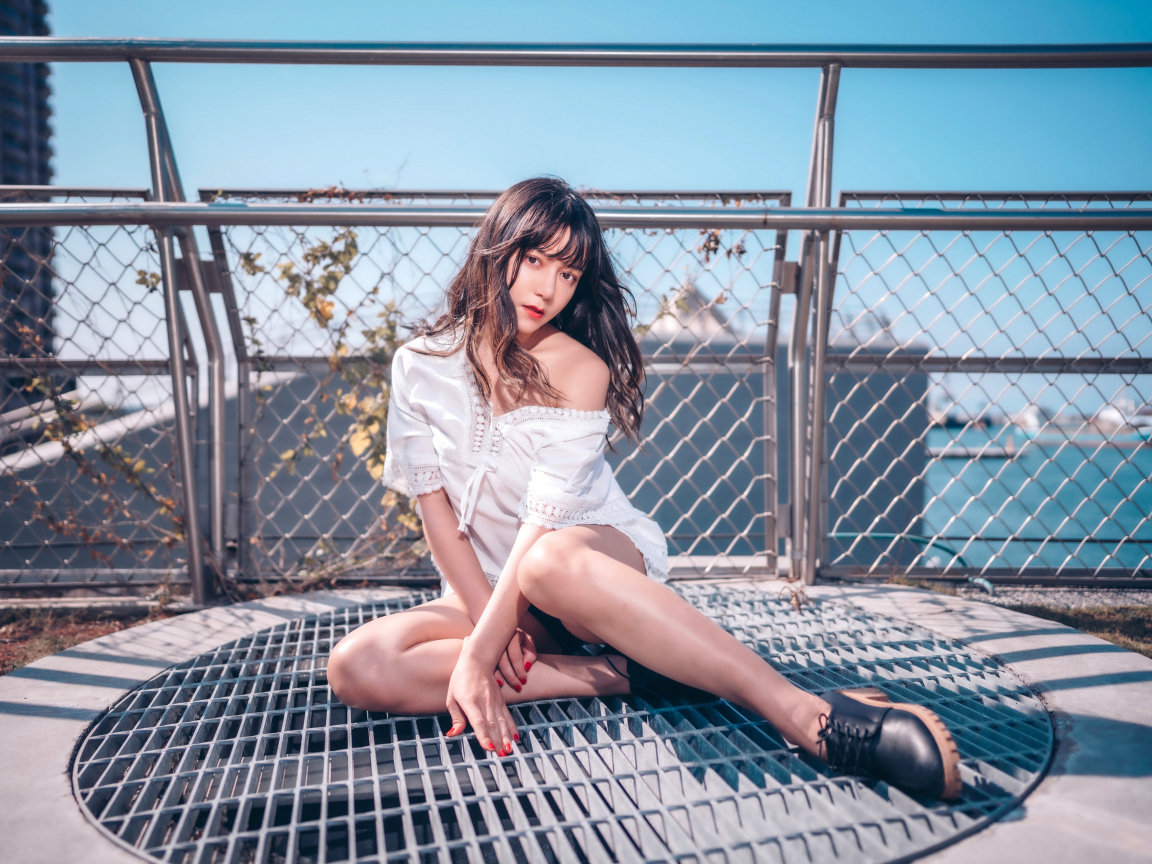 Девушка азиатка в белом наряде сидит на сетке