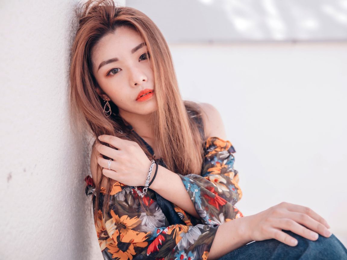 Девушка азиатка сидит на полу у стены 