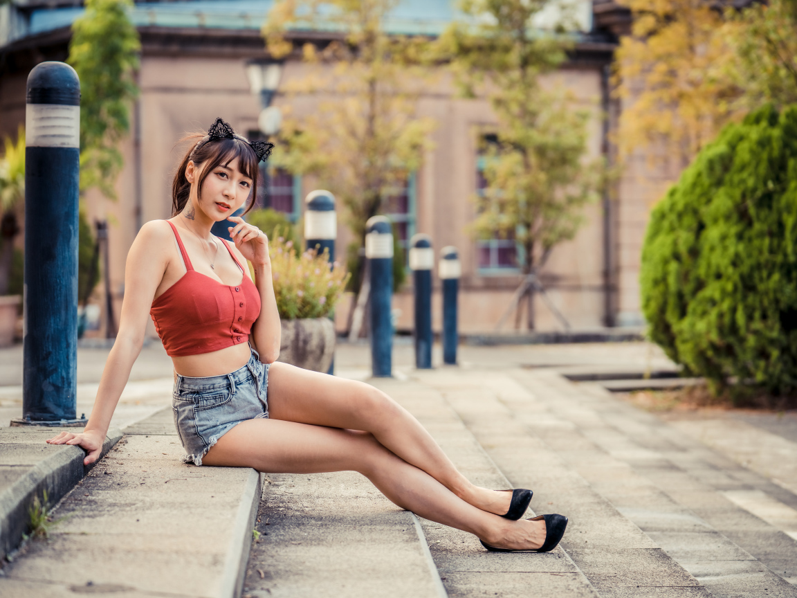 Азиатка в шортах сидит на ступенях 