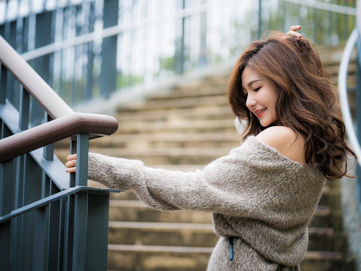 Красивая девушка азиатка в сером свитере на ступеньках 