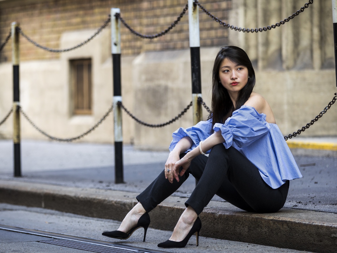 Красивая девушка азиатка в черных брюках сидит на земле