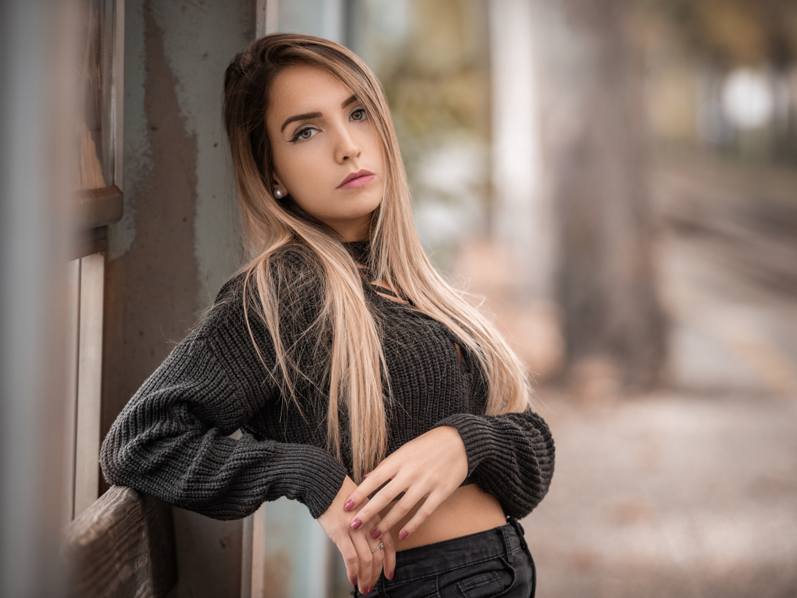 Красивая блондинка в вязаном свитере у стены 