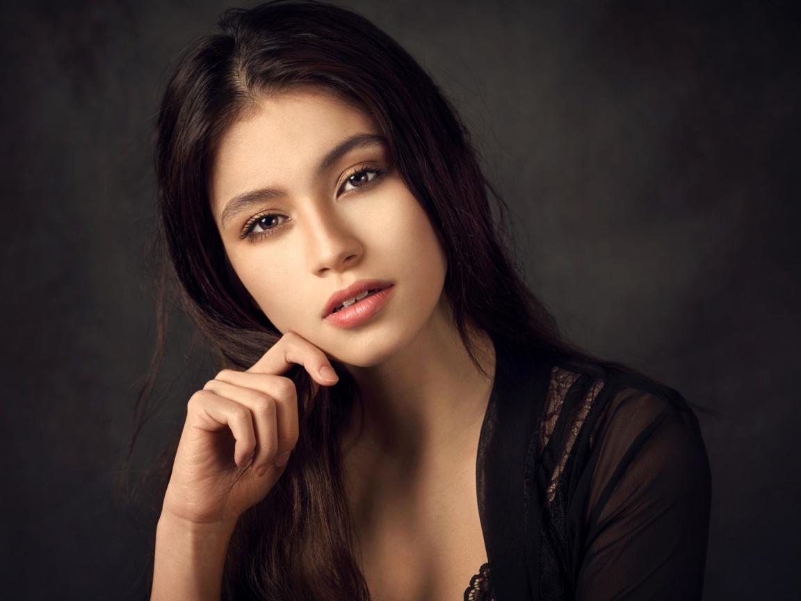 Красивая девушка в черном сидит на сером фоне