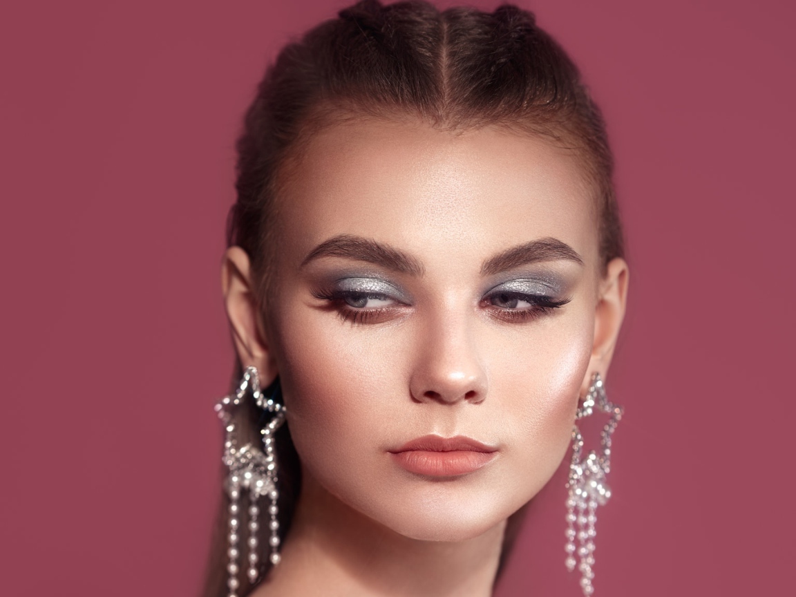 Красивая девушка с макияжем и большими серьгами на розовом фоне