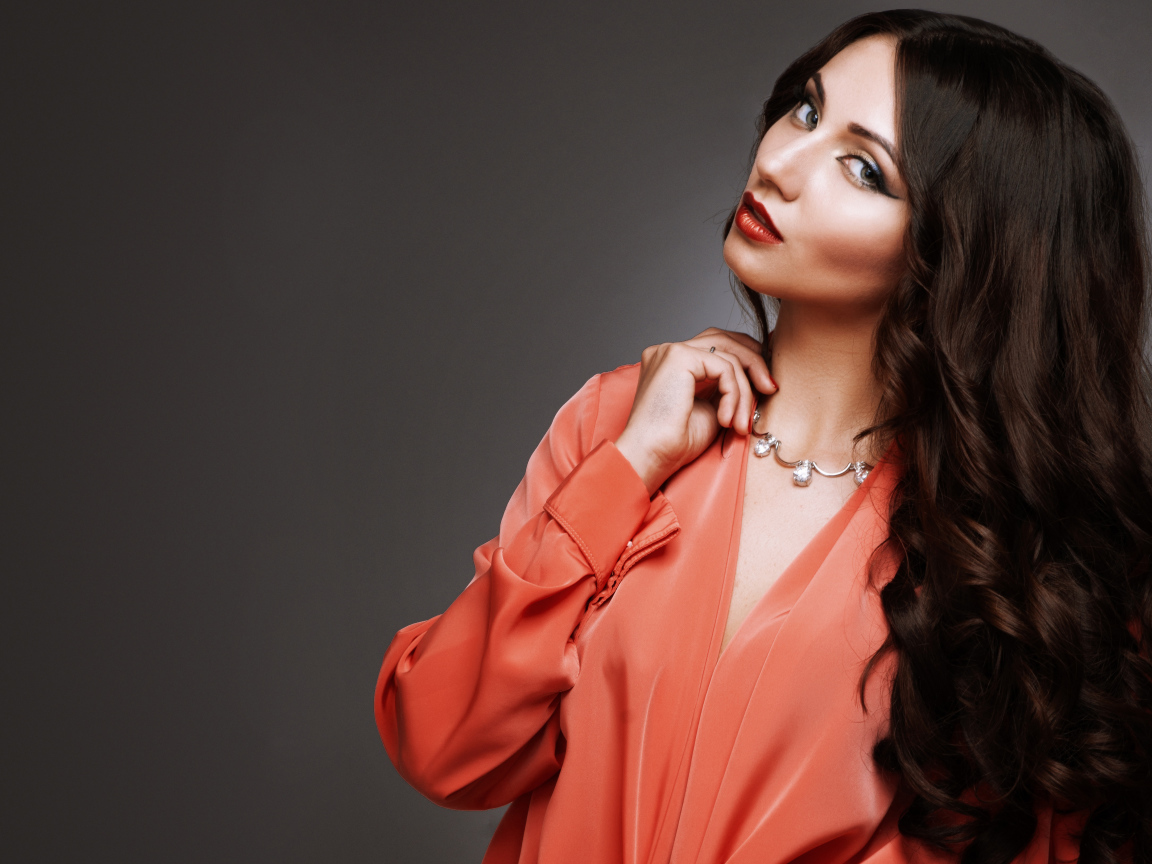 Красивая длинноволосая девушка в красной рубашке на сером фоне 