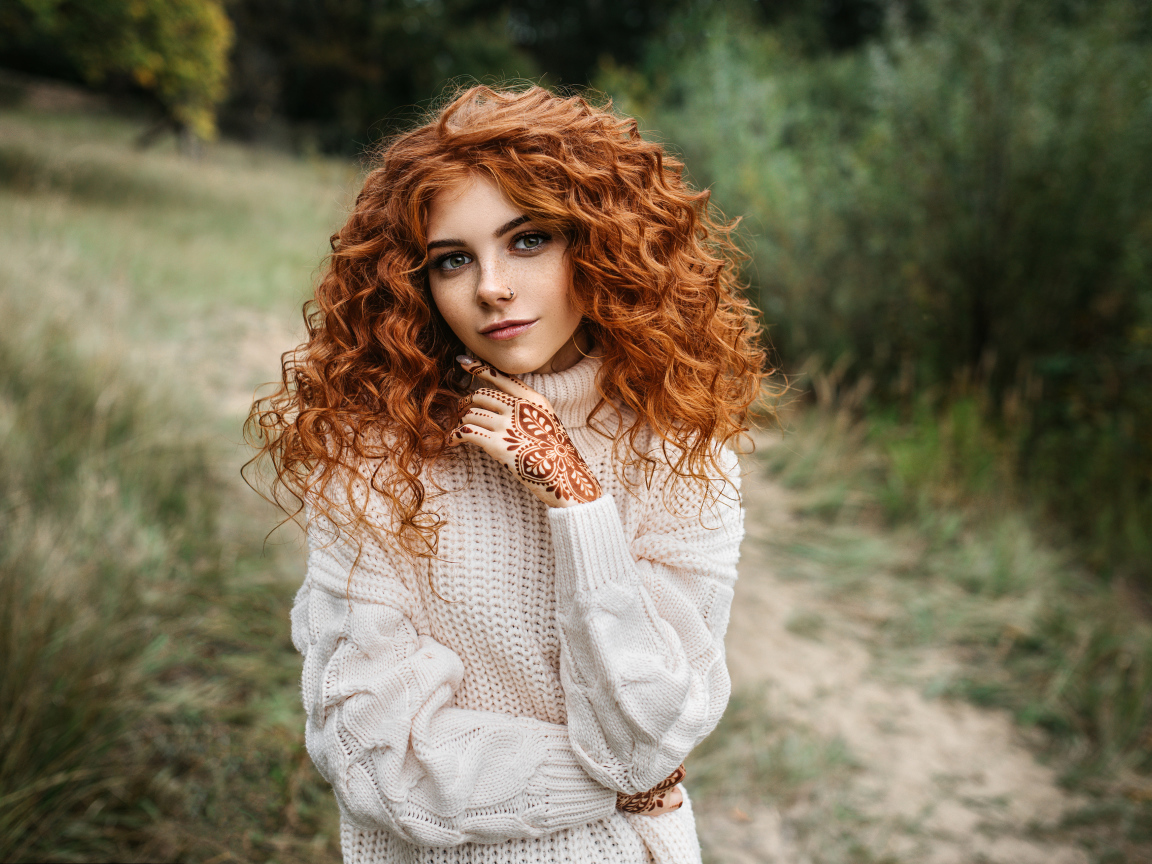 Красивая рыжеволосая девушка в белом свитере с рисунками из хны на руках