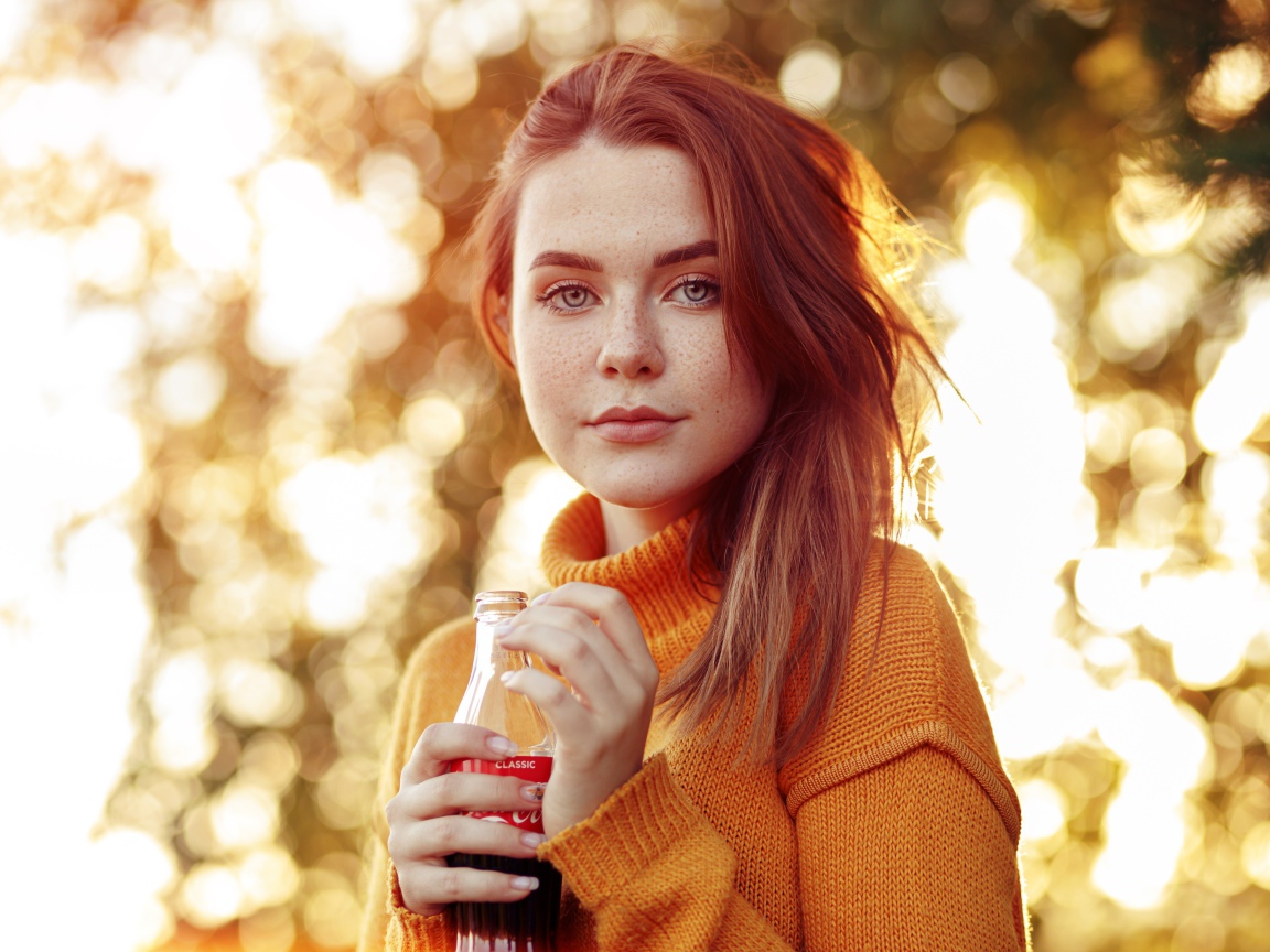 Красивая рыжеволосая девушка с бутылкой кока колы в руке 