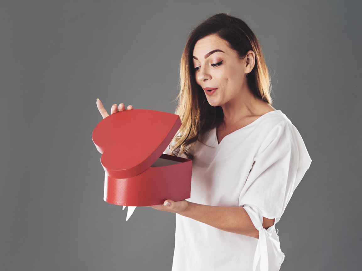 Любопытная девушка смотрит в красную коробку в форме сердца