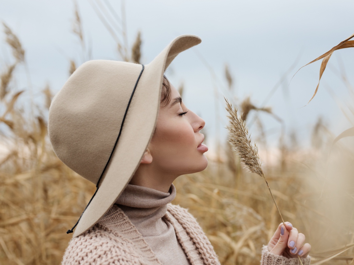 Девушка в шляпе с закрытыми глазами держит колосок 