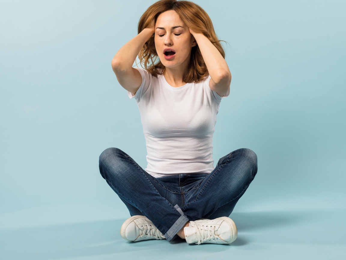 Девушка с руками в волосах сидит в джинсах на голубом фоне