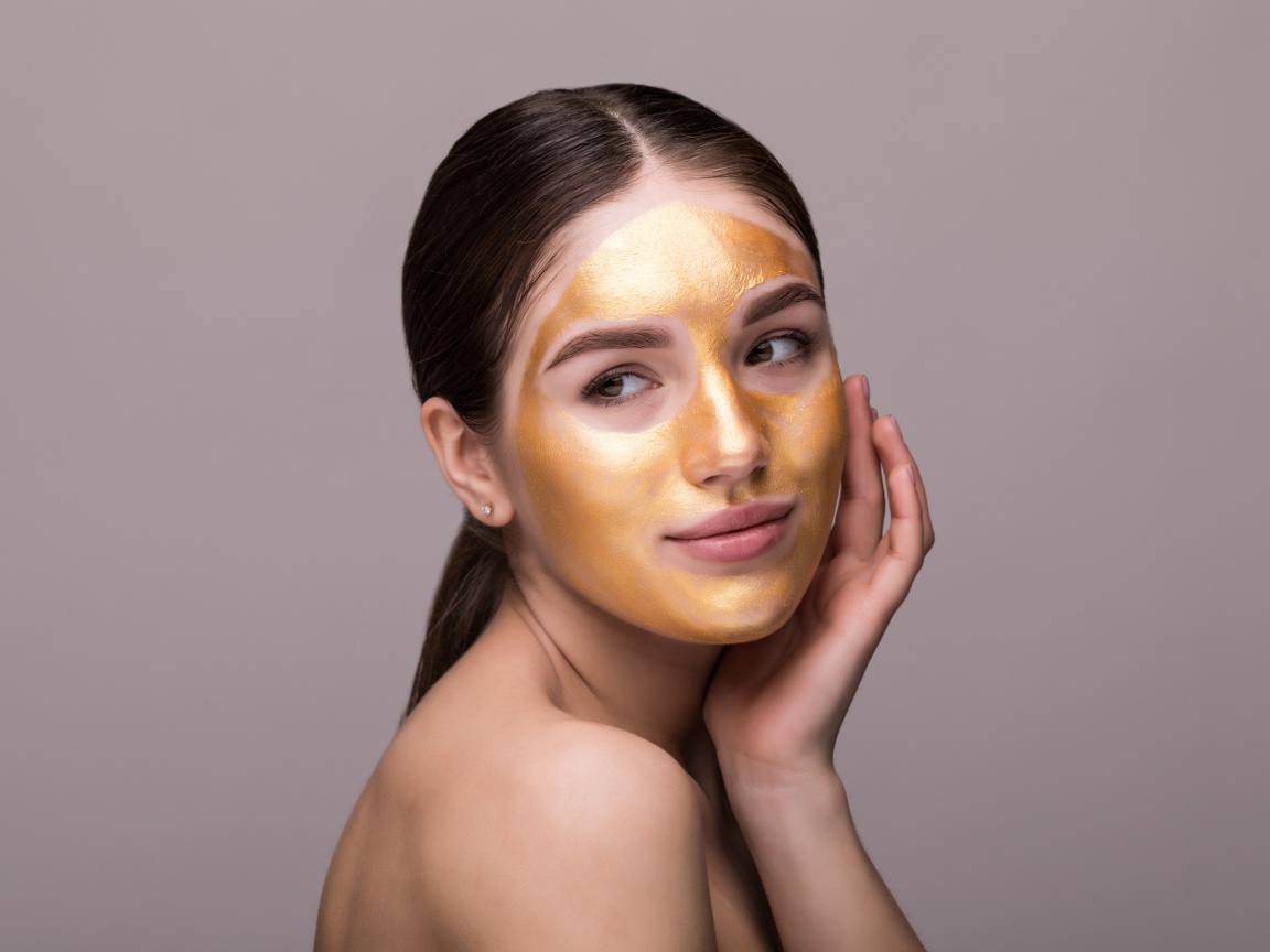 Золотая маска на лице у молодой девушки 