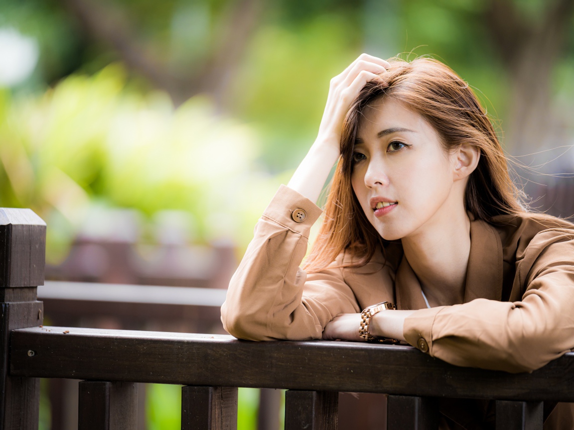 Грустная девушка азиатка стоит у деревянных перил 