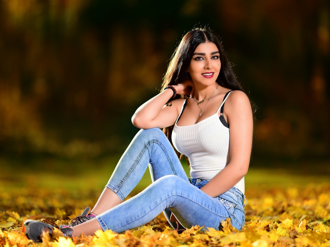 Улыбающаяся брюнетка сидит на опавшей листве