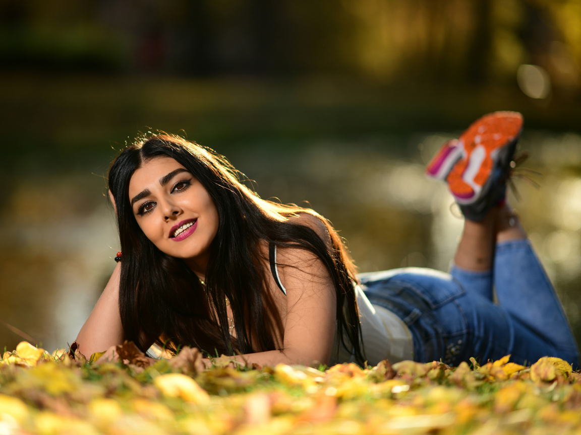 Smiling girl model lies on the ground with fallen leaves