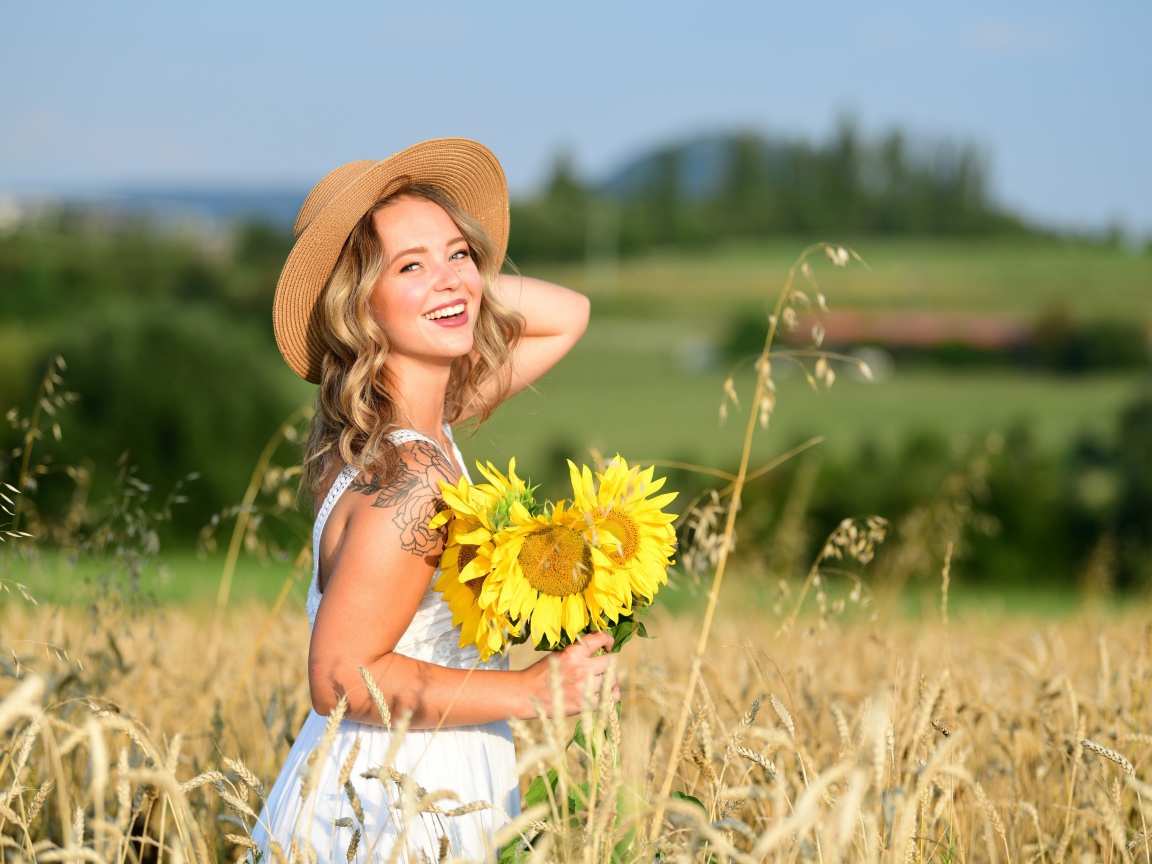 Улыбающаяся девушка с букетом подсолнухов на поле пшеницы
