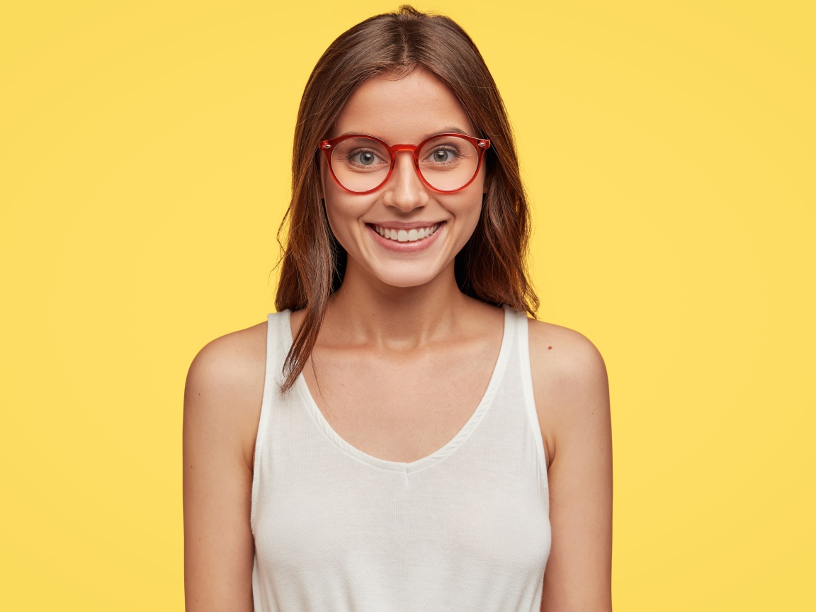 Улыбающаяся девушка в очках на желтом фоне 