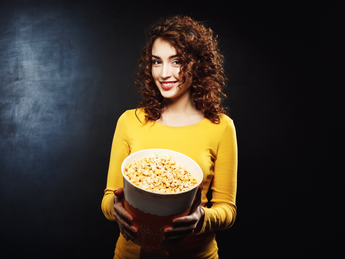 Улыбающаяся девушка с попкорном в руках на черном фоне 