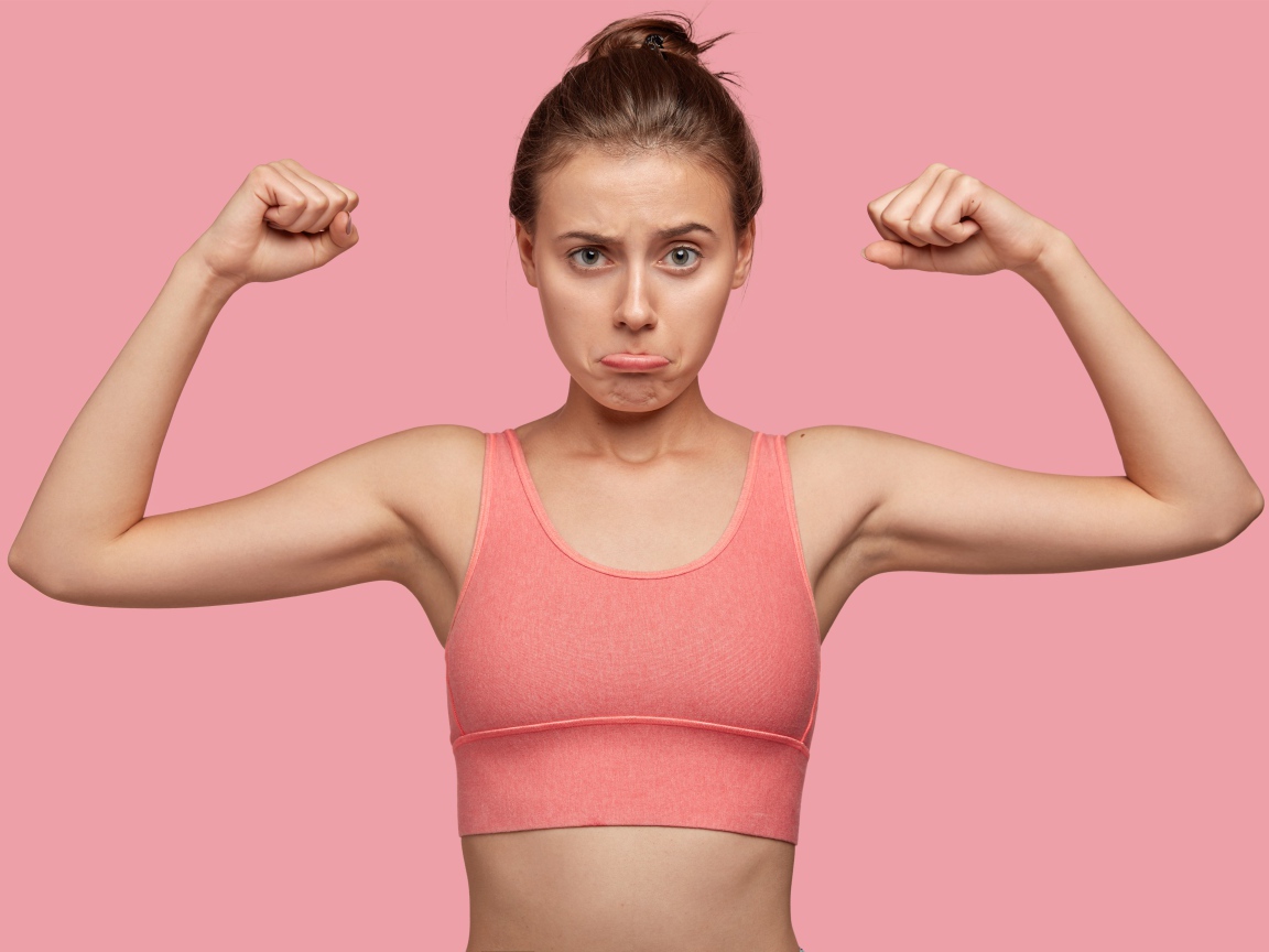 Расстроенная девушка без накаченных рук на розовом фоне