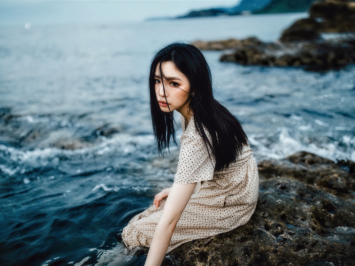 Молодая девушка азиатка сидит на камне у воды