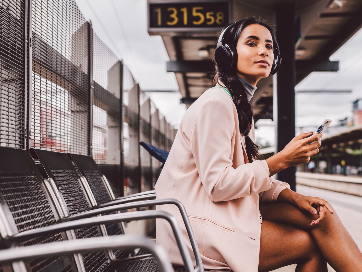 Молодая девушка в наушниках сидит на остановке