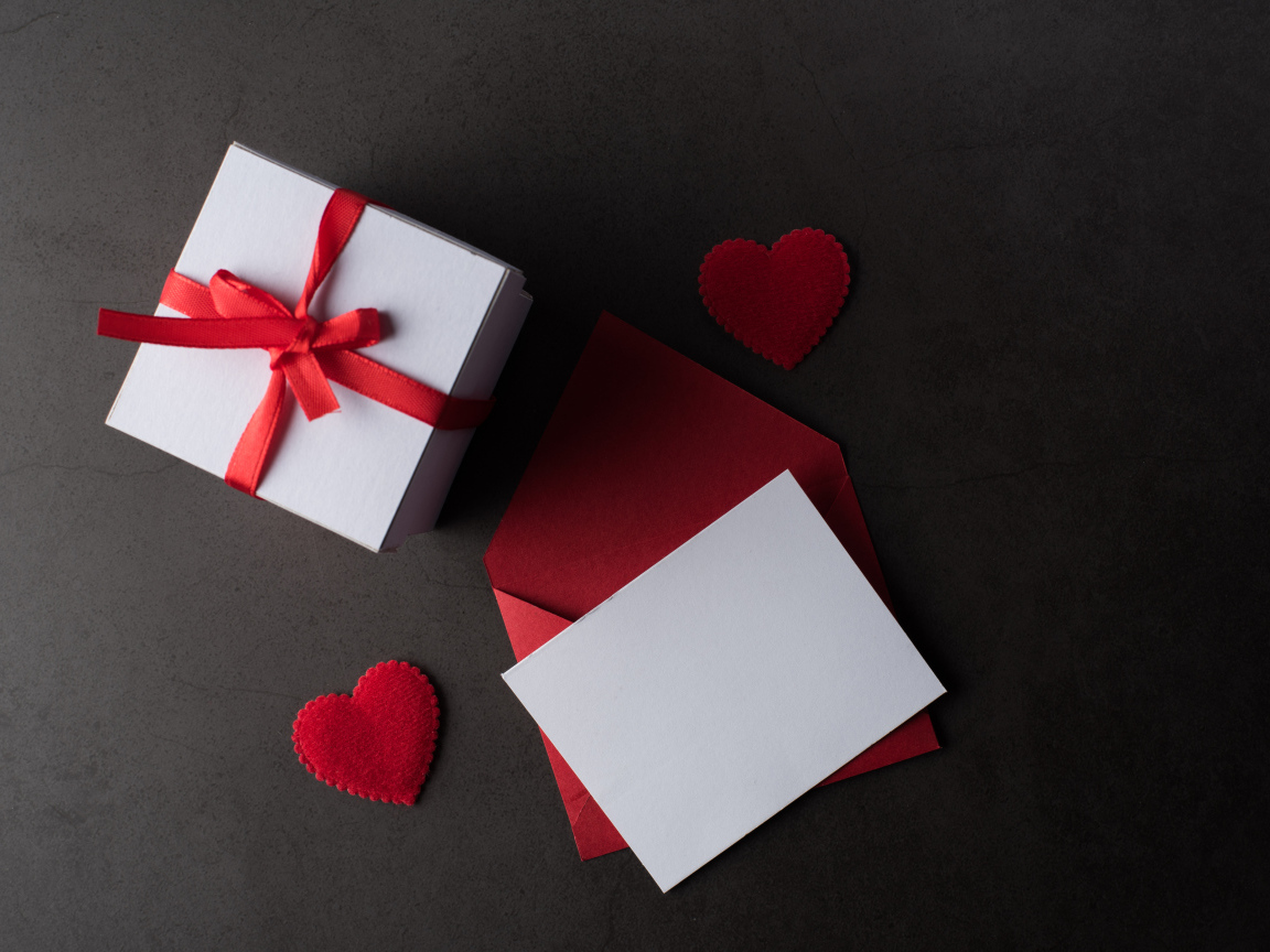 Конверт и подарок на сером столе с красными сердечками