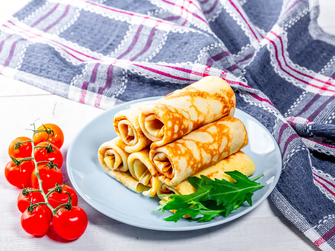 Блинчики на столе с помидорами и полотенцем угощение на Масленицу 2020