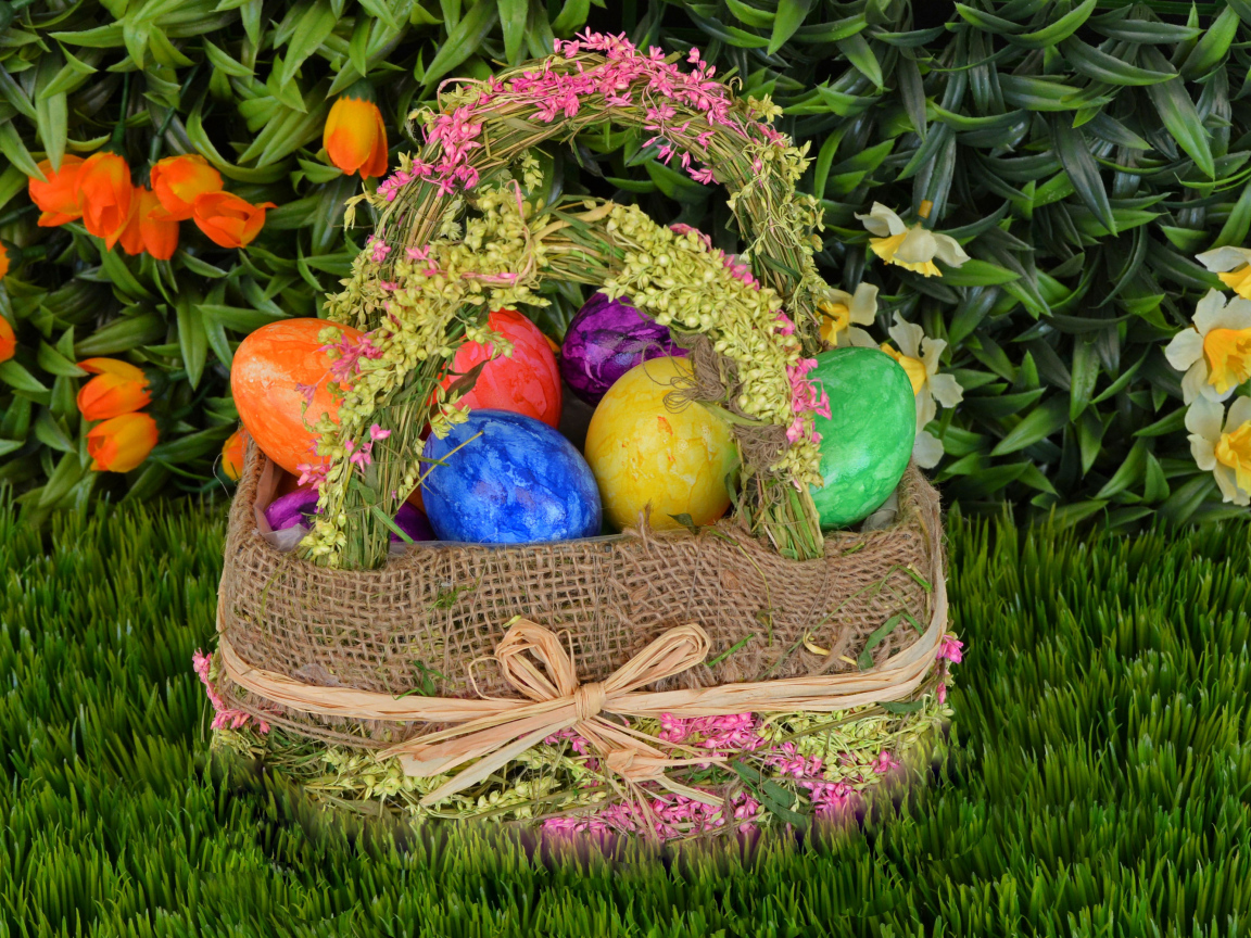 Разноцветные пасхальные яйца в корзине на зеленой траве на праздник 