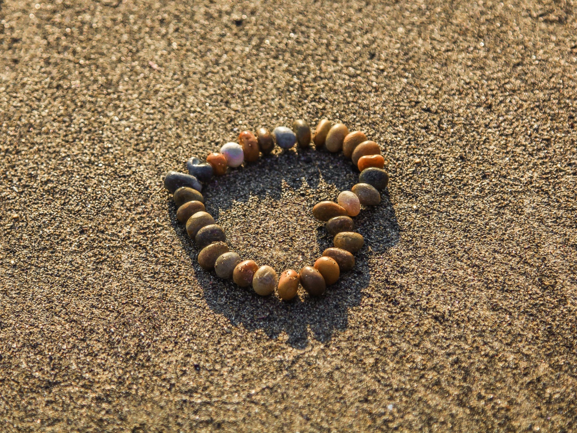 Сердце из мелкий морских камей на песке 