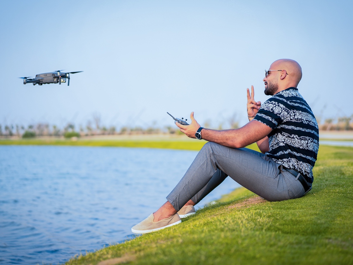 Мужчина запускает квадрокоптер над озером 