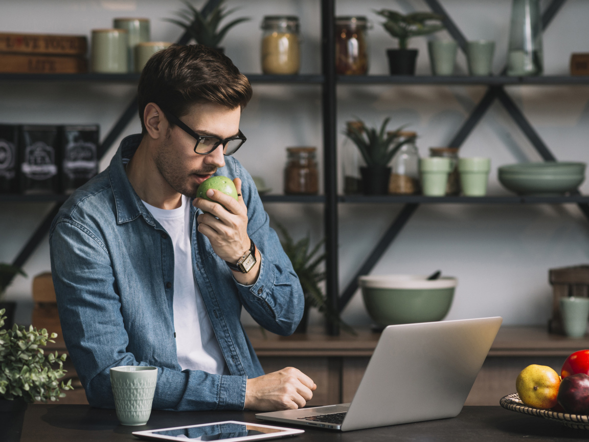 Мужчина с ноутбуком ест яблоко в кафе 