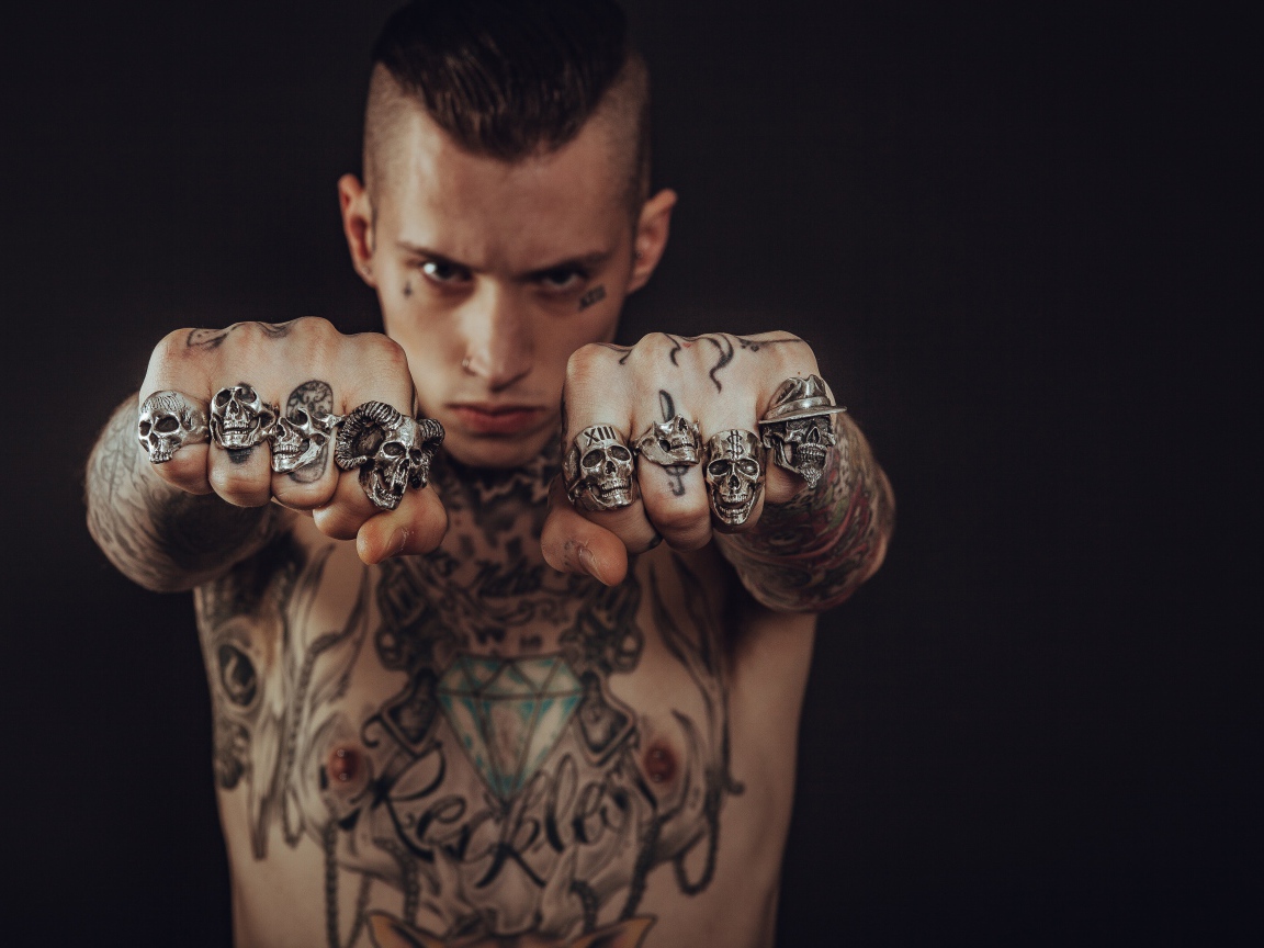 Мужчина с татуировками на теле с перстнями на пальцах