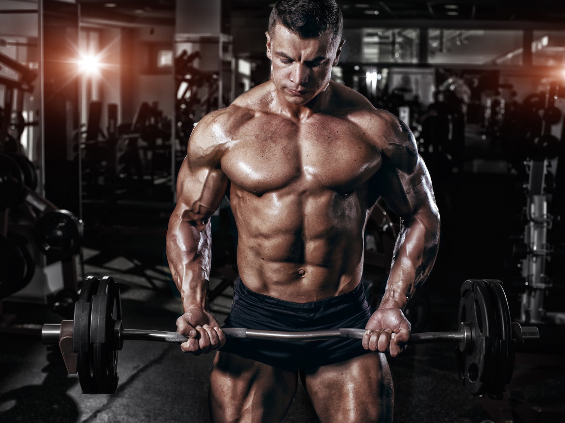 Мускулистый мужчина со штангой в руках в спортзале