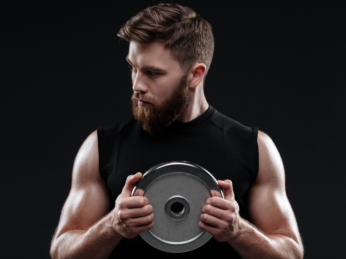 Молодой накаченный парень с железным диском на черном фоне