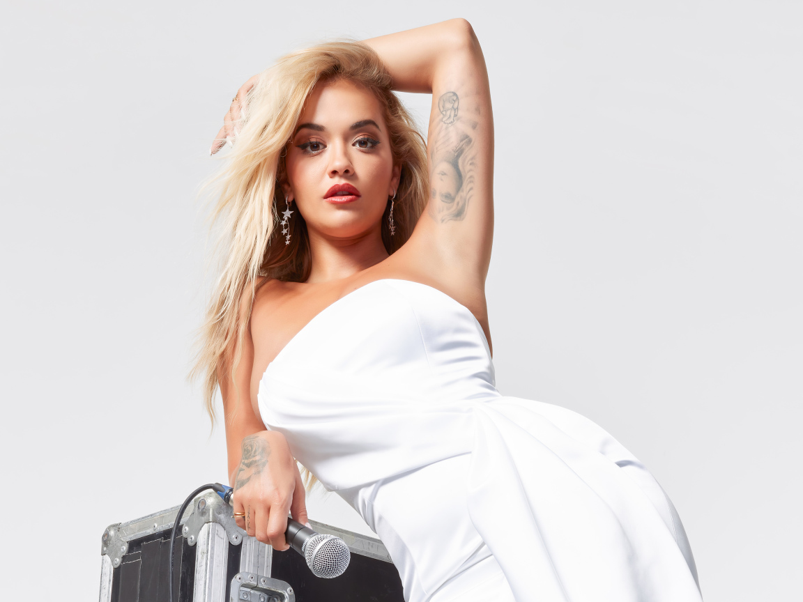 Певица Рита Ора в белом платье с микрофоном