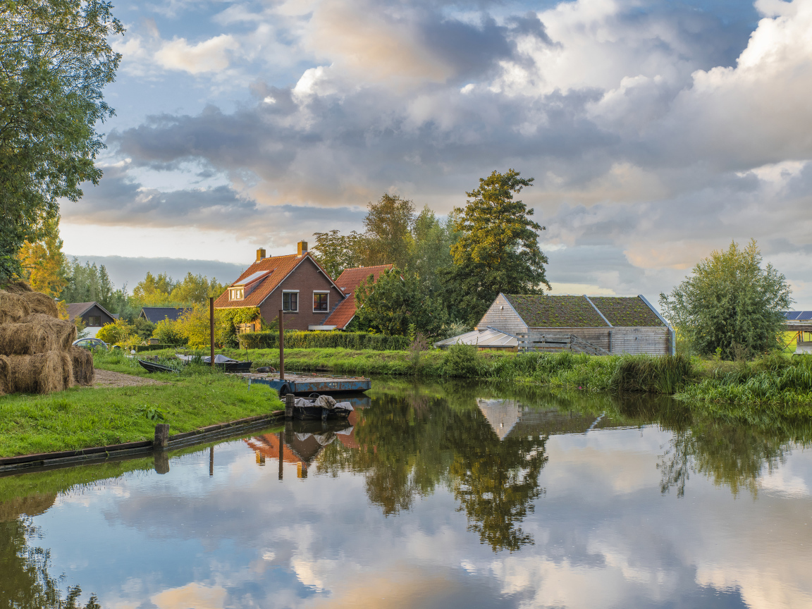 Дома отражаются в реке под небом с белыми облаками