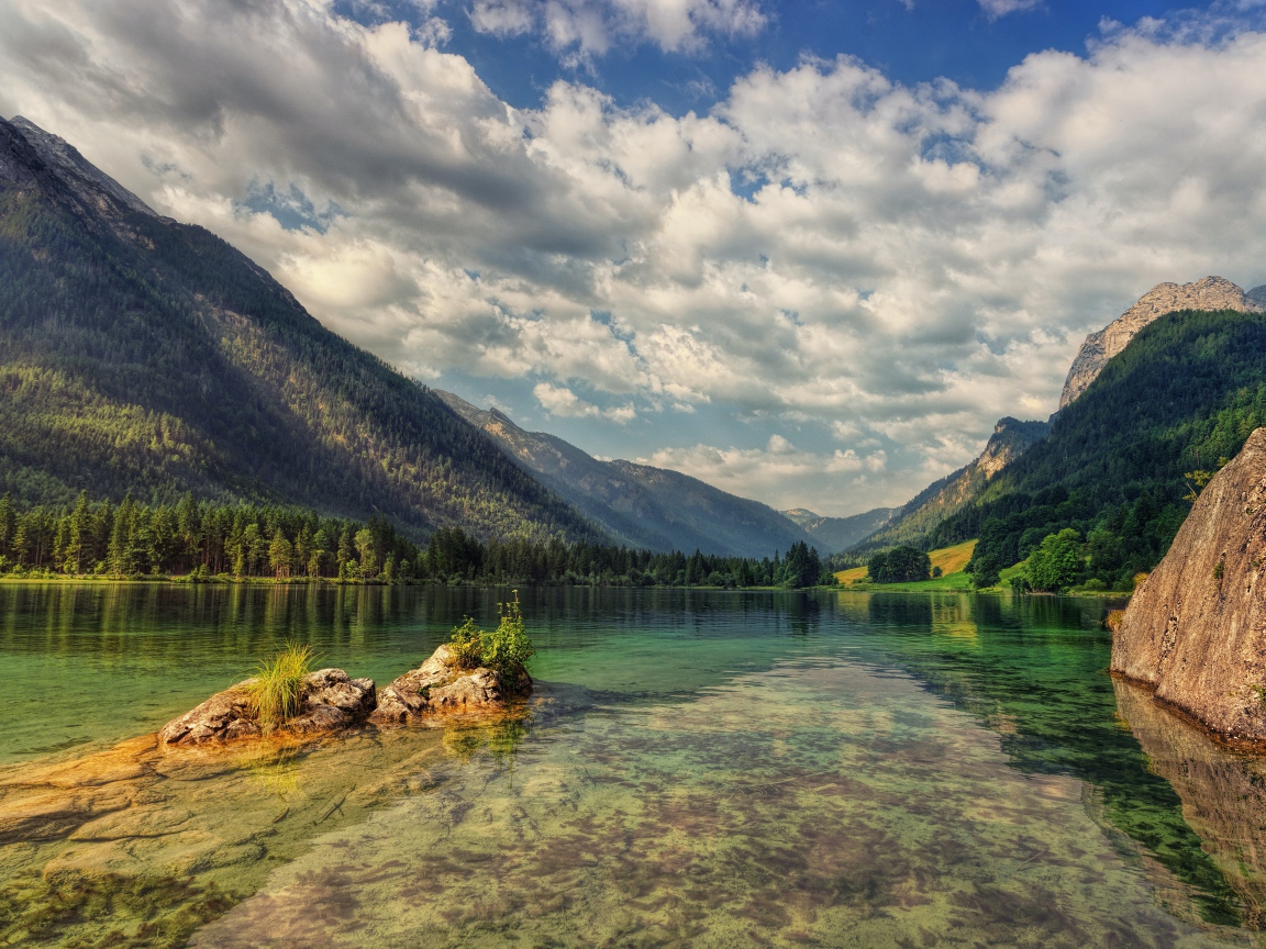 Большие камни в озере на фоне гор под небом с белыми облаками