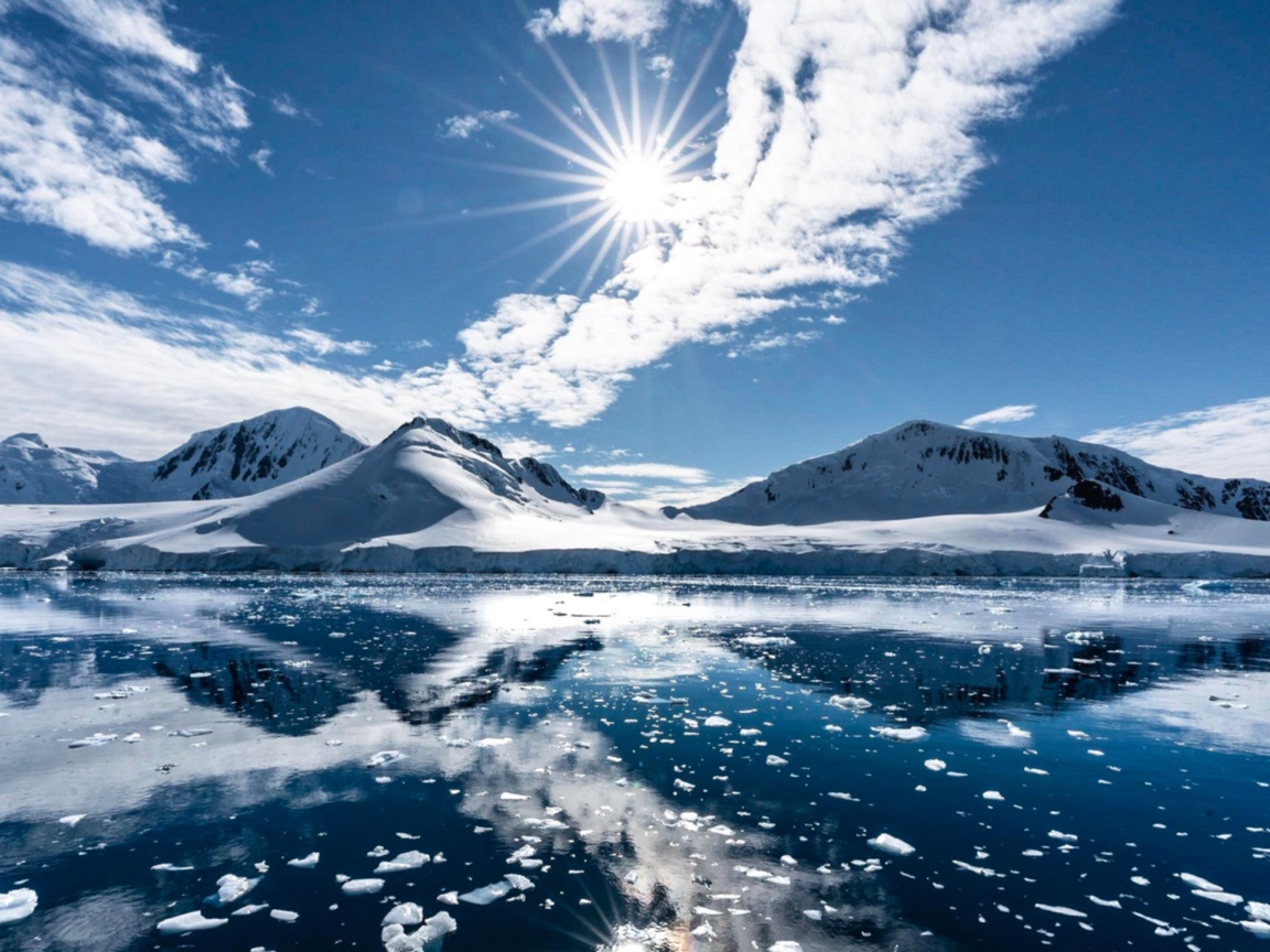 Белые облака в солнечном небе отражаются в озере у заснеженных гор 