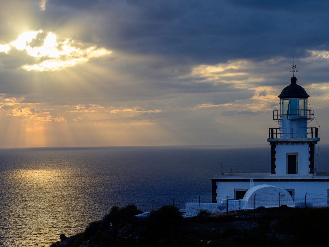 Белый маяк на берегу в лучах солнца у моря 
