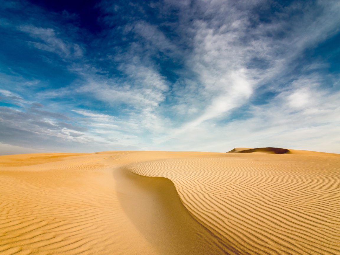 Песчаная дюна под голубым небом с белыми облаками 