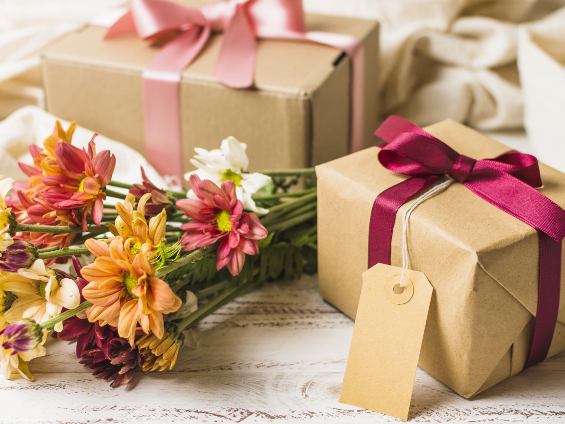 Букет разноцветных хризантем с подарками на столе 